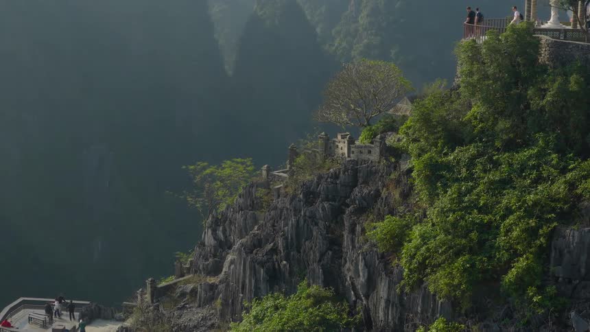 Tourists and a wedding couple stand on a scenic clifftop viewpoint overlooking the misty limestone mountains of Ninh Binh, Vietnam
