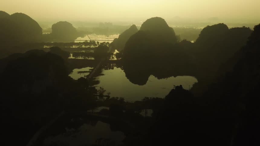 A stunning aerial view of a misty valley with silhouetted mountains and tranquil lakes during a golden sunrise