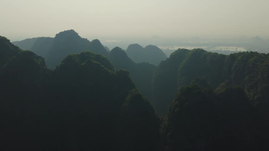 A stunning panoramic view shows a vast landscape of lush green mountains stretching to the horizon under a hazy sky