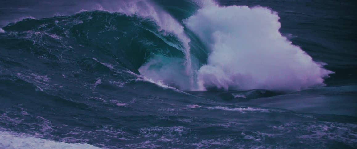 A powerful, dark ocean wave crests and barrels in dramatic slow motion, churning up white water spray