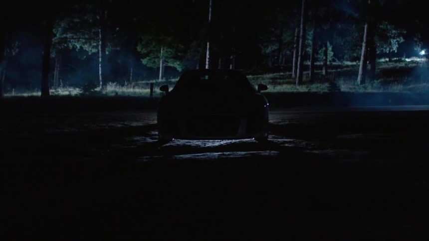 A car sits in the dark, then it's headlights come on
