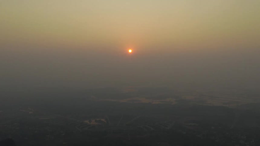 The sun glows through a thick, hazy atmosphere, casting a warm light over a smog-covered landscape below