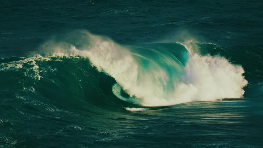 A giant, mesmerizing turquoise wave curls and crashes in the open ocean in super slow motion