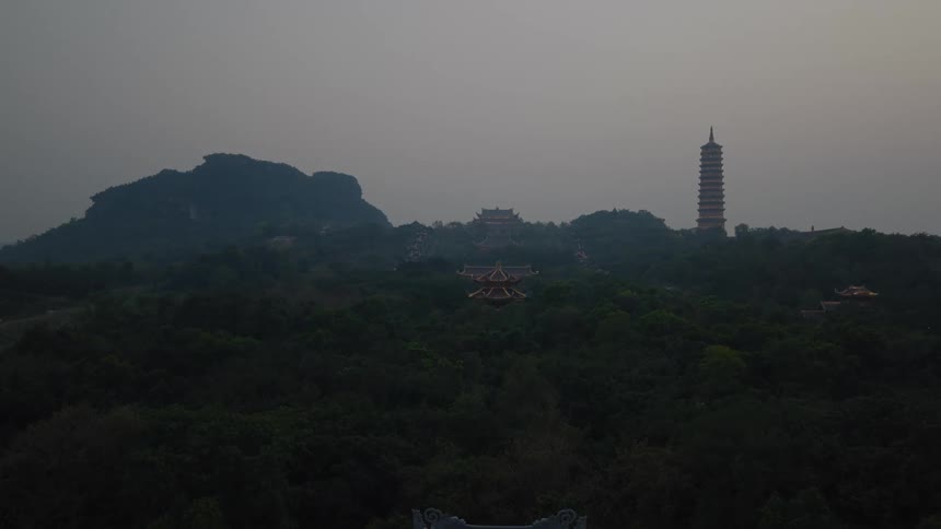 The sprawling Bai Dinh Pagoda complex sits amongst the forested mountains of Vietnam under a hazy, dusky sky