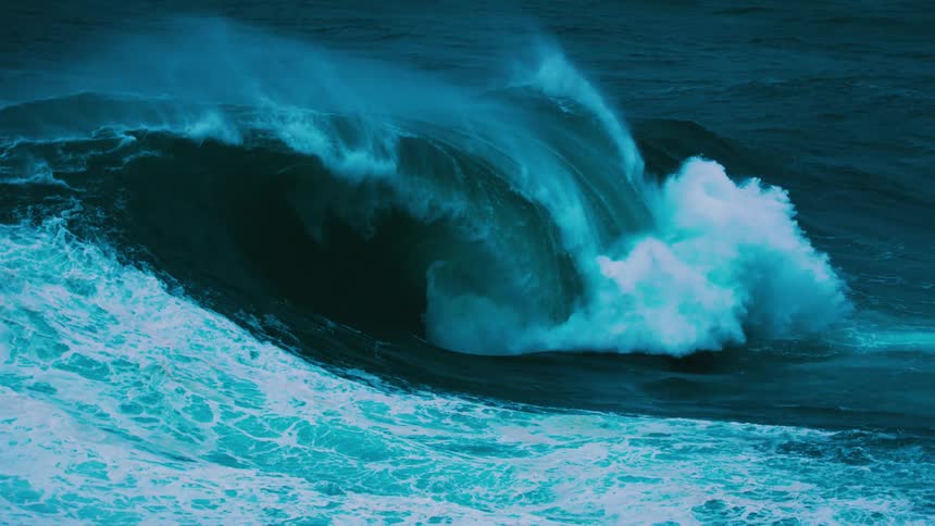 Slow motion footage shows a massive turquoise ocean wave forming a barrel and crashing with immense force