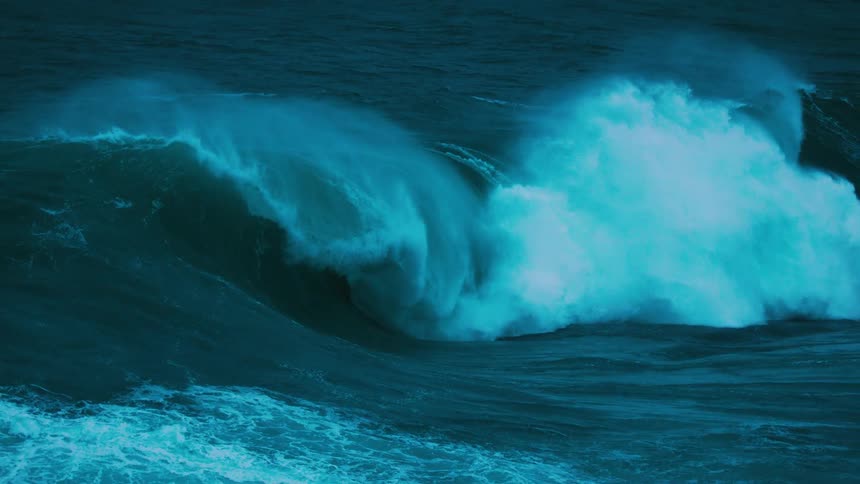 An immense, dark teal ocean wave builds momentum before crashing in dramatic super slow motion