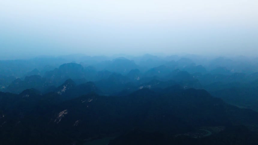 A vast landscape of misty blue mountains fades into the horizon at dusk