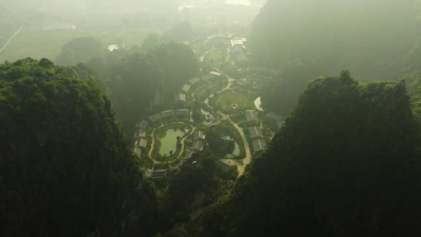 High aerial view of a secluded resort village nestled within a misty, green mountain valley