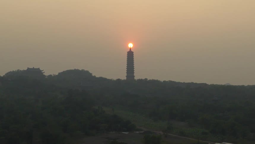 A stunning time-lapse captures the sun rising directly behind a tall pagoda, creating a beautiful silhouette against the hazy morning sky