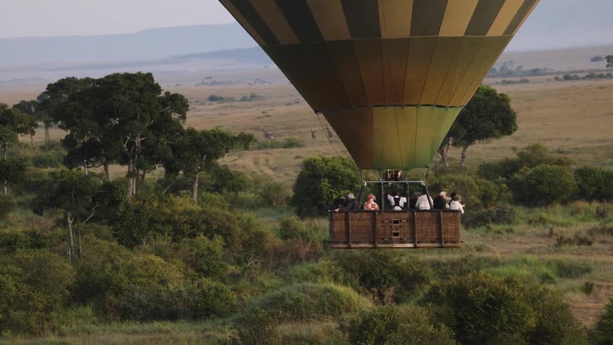 A hot air balloon carrying tourists on a safari drifts slowly over the lush green plains of the African savanna