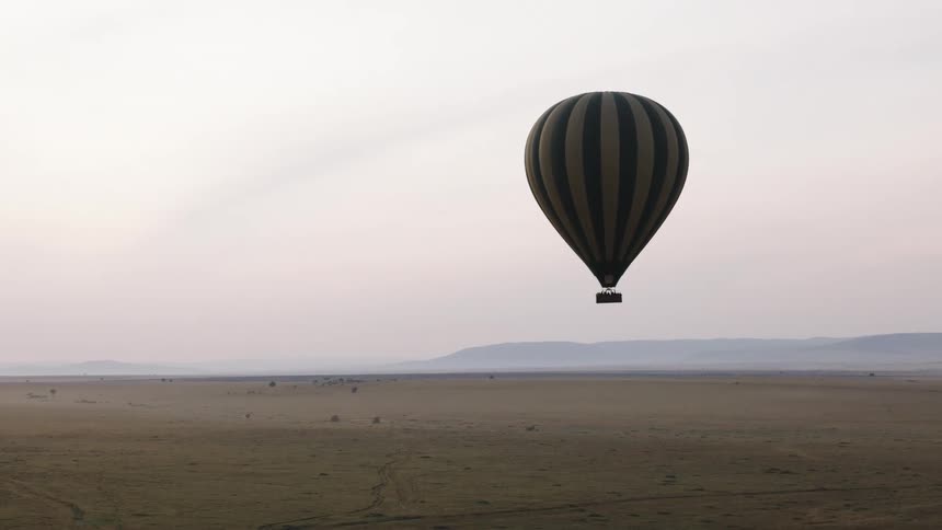 A solitary hot air balloon peacefully floats over the vast, hazy African savanna at dawn