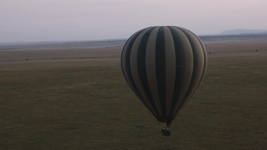 A green and beige striped hot air balloon peacefully floats over the expansive savanna at dawn