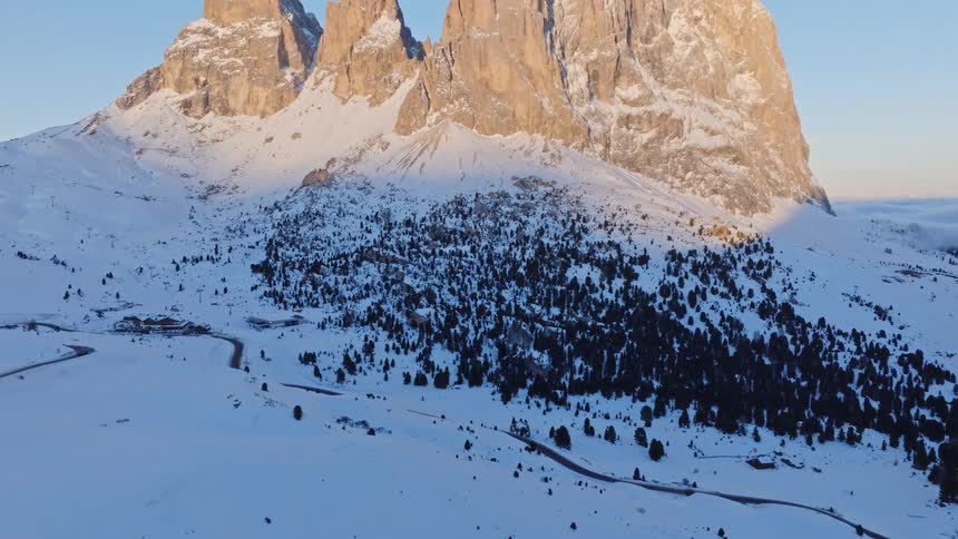 A stunning aerial view tilts up to reveal a majestic snow-covered mountain range illuminated by the warm glow of sunrise