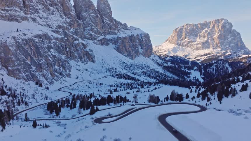 A stunning aerial view of cars driving on a winding mountain road through a breathtaking snowy valley in the Alps at sunrise