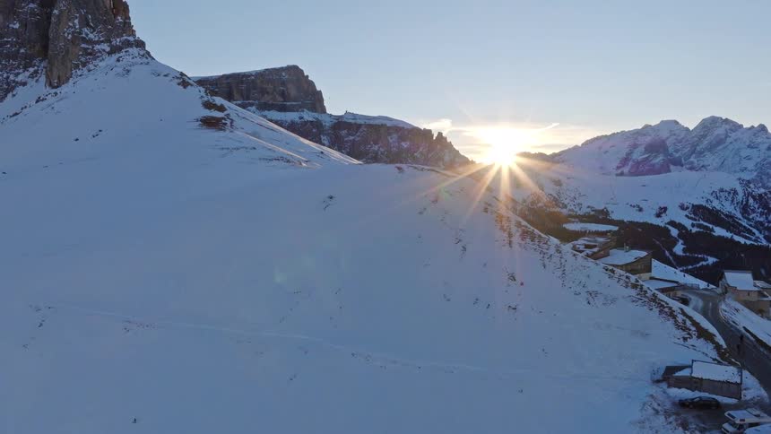 A stunning aerial view captures the sunrise over a vast, snow-covered mountain range, with a road winding through the valley below