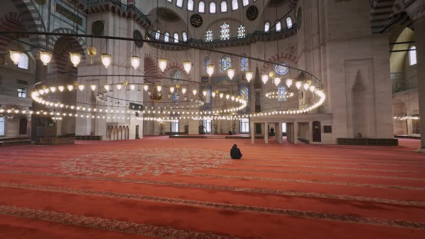 A lone person prays in solitude on the vast red carpet inside a majestic and historic mosque