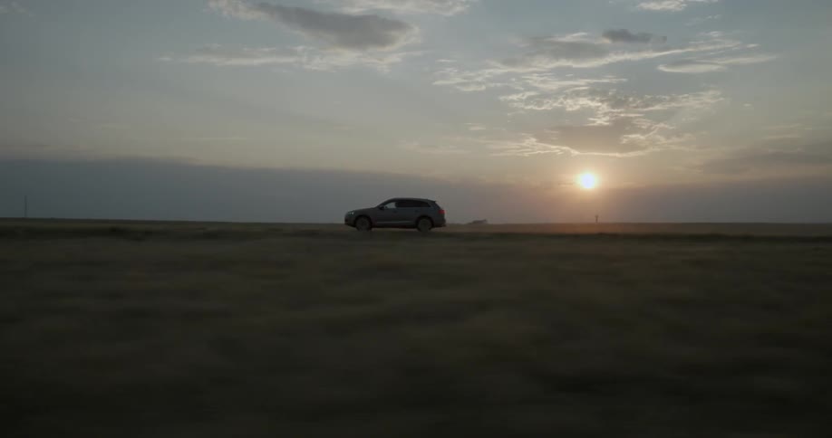 A car drives across an open field at sunset