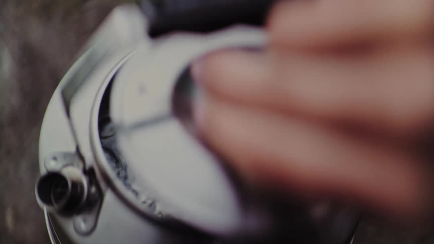 A person removes the lid from a steaming metal kettle, revealing the boiling water inside