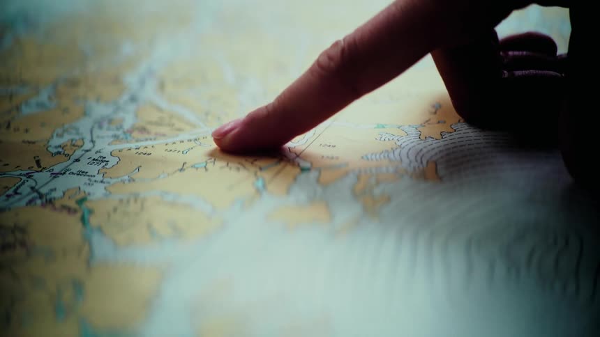 A person's finger traces a route across a detailed nautical chart, carefully planning an upcoming voyage
