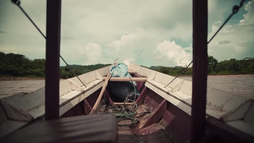 Point of view from a traditional wooden boat floating down a wide river through a lush, remote jungle