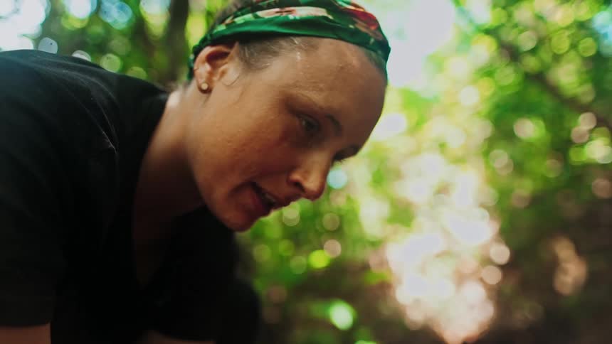 A woman hiking in the forest bends down to a stream to wash her face with cool water in slow motion