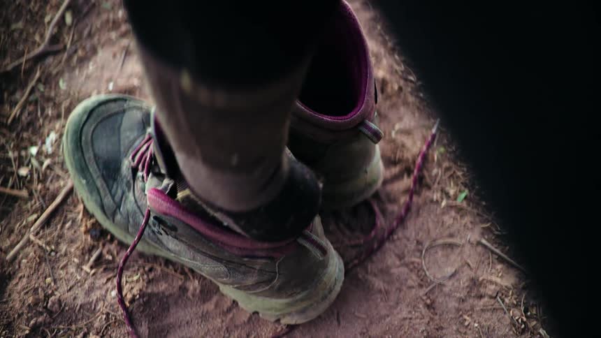Slow motion close-up of a hiker putting on a muddy hiking boot on a dirt trail