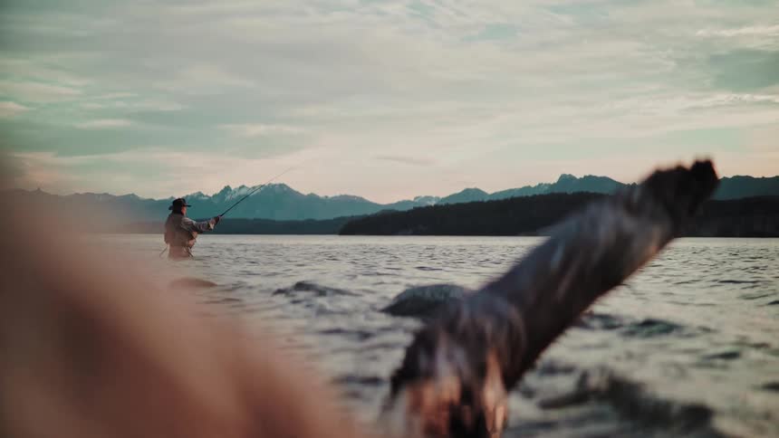 A solitary fisherman casts a line while fly fishing in a tranquil mountain lake at sunset