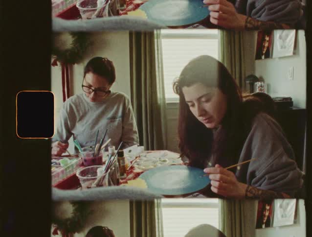 Two women quietly paint together at a table in a cozy room, captured on vintage-style film