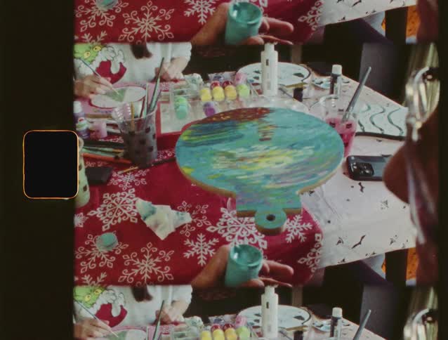 A multi-frame vintage film captures a close-up of a festive table where people are painting Christmas ornaments together
