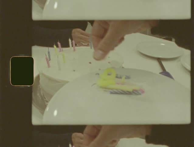 Vintage home movie footage shows hands placing candles on a white frosted birthday cake in a distorted, kaleidoscopic view