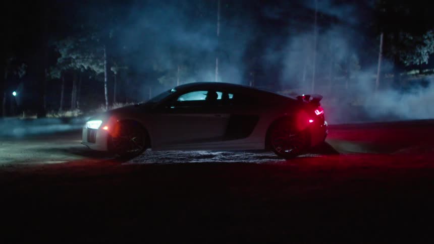 Fog blows around a car parked in the woods at night