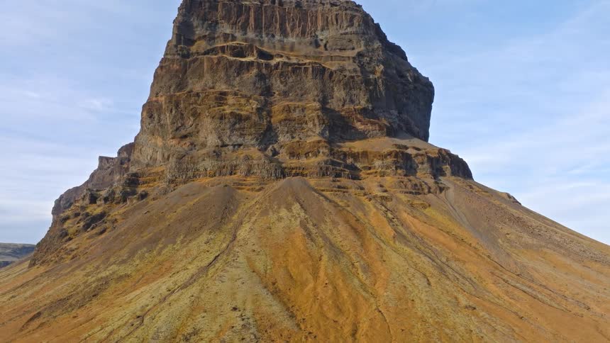 An aerial view slowly ascends a majestic and rugged mountain in the Icelandic highlands