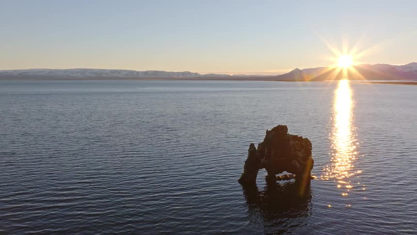 Aerial footage reveals the iconic Hvitserkur sea stack in Iceland, beautifully silhouetted against a golden sunset over the calm sea