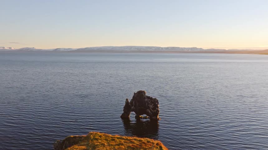 A slow pan reveals the majestic Hvitserkur basalt sea stack in Iceland's Huna Bay as the sun rises over the distant mountains