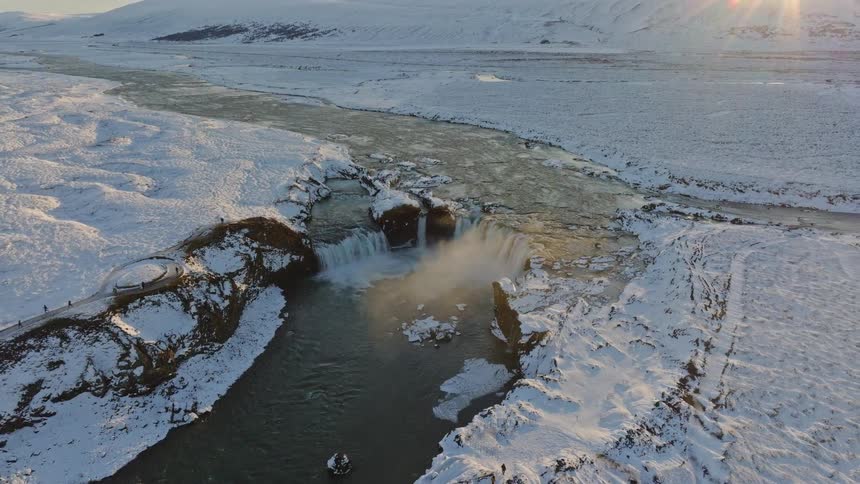 Stunning aerial pull-back shot of the magnificent Godafoss waterfall surrounded by a vast, snow-covered Icelandic landscape at sunrise