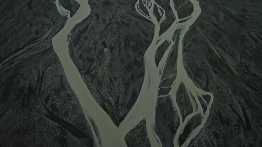 A stunning top-down aerial shot pulls back to reveal an intricate braided river system flowing through a vast volcanic landscape