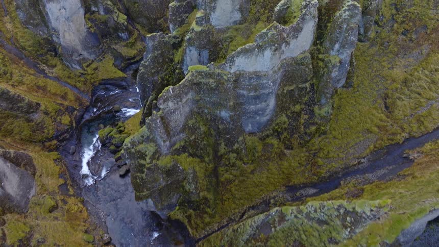 A dramatic top-down aerial shot slowly tilts up to reveal the vast, moss-covered cliffs of a majestic canyon and the river winding through it