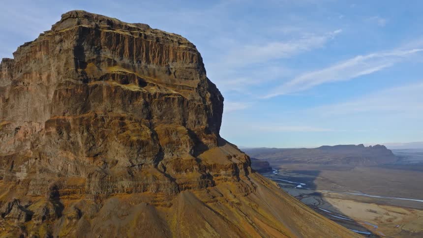 A slow aerial pullback reveals a majestic, flat-topped mountain overlooking a vast, remote river valley in Iceland
