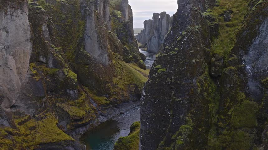 A stunning aerial view pulls back through the deep, moss-covered Fjaðrárgljúfur canyon as a river winds through its dramatic landscape in Iceland