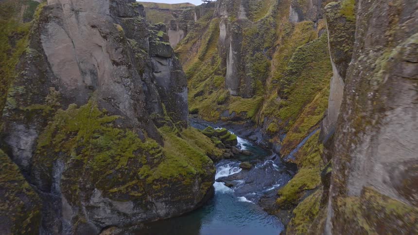 An epic aerial flight deep into a majestic green canyon as a winding river flows through the rocky landscape of Iceland