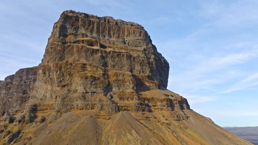 A dramatic aerial shot pulls back slowly from a massive, solitary volcanic mountain to reveal the vast, barren highlands of Iceland
