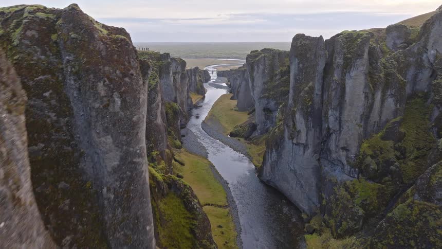 An aerial drone shot flies slowly through a majestic green canyon, revealing a river flowing through the valley in Iceland