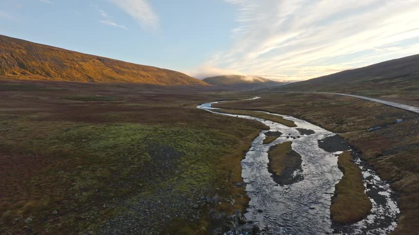 An aerial view flies over a winding river through a vast Icelandic valley during a golden sunrise