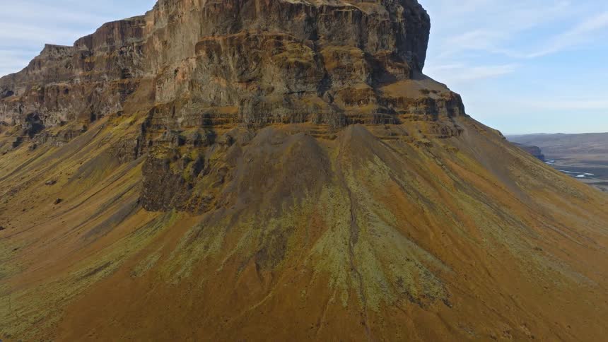 A slow aerial tilt-up reveals the immense and rugged beauty of a solitary mountain in the vast, open landscape of Iceland