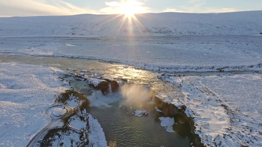 Breathtaking aerial view of a majestic waterfall cascading through a vast, snow-covered landscape in Iceland during a golden sunrise