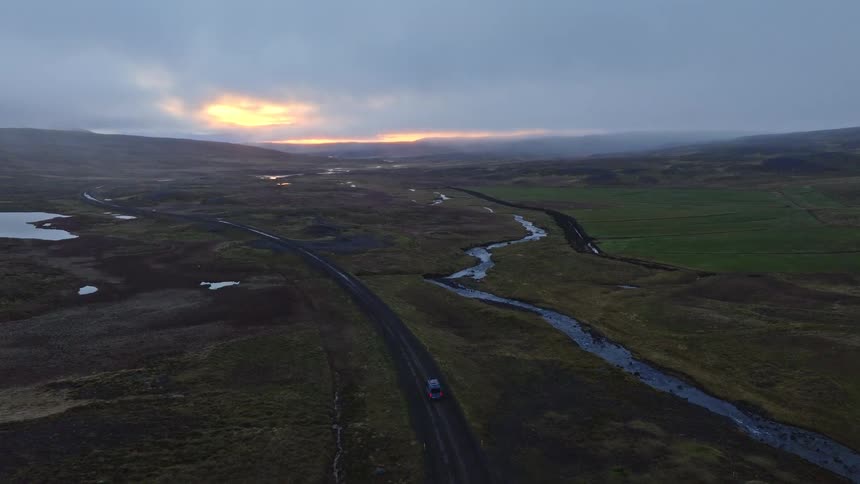 Aerial view of a car driving on a remote road through the vast Icelandic landscape at sunrise
