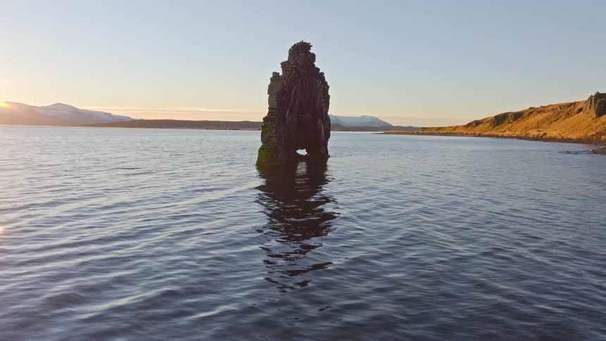A stunning aerial view captures the sun rising behind the iconic Hvítserkur sea stack in Iceland, creating a beautiful sunburst over the calm water