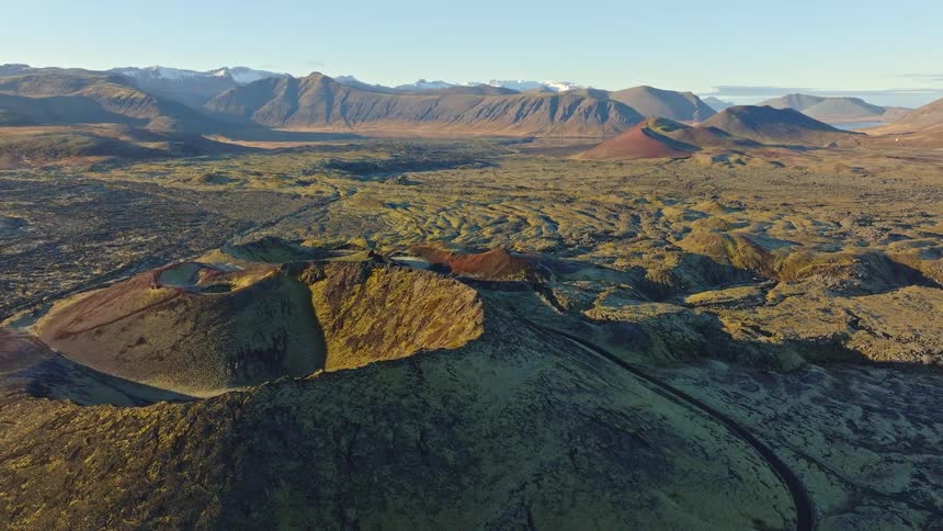 Aerial view retreating from a moss-covered volcanic crater in a vast Icelandic landscape during golden hour