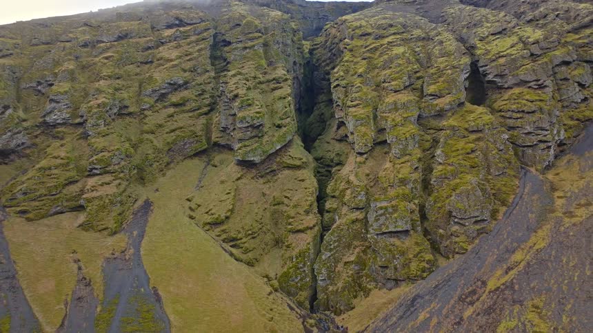 An epic aerial pullback reveals a massive mossy green canyon carved into the rugged, volcanic mountains of Iceland