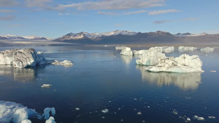 A majestic aerial view captures serene icebergs floating in a vast glacial lagoon with snowy mountains in the background